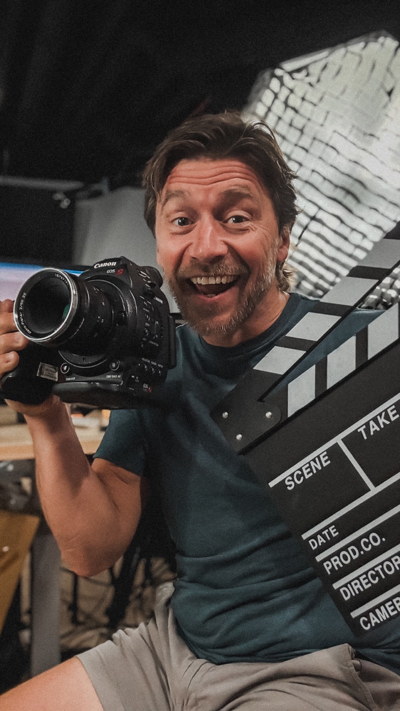 Ryan Koral, founder of Tell Studios, holding a camera and clapperboard in the studio
